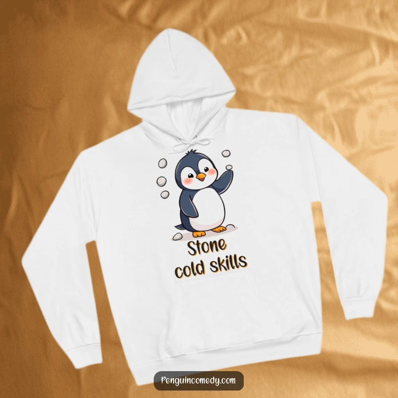 Funny penguin character in the act of juggling three small pebbles, captured in a whimsical design on a warm hoodie.